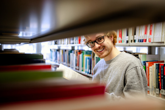 Bücherrecherche in der Bibliothek Ein Studierender steht an einem Bücherregal in der Bibliothek.