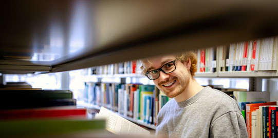 Ein Studierender steht an einem Bücherregal in der Bibliothek.